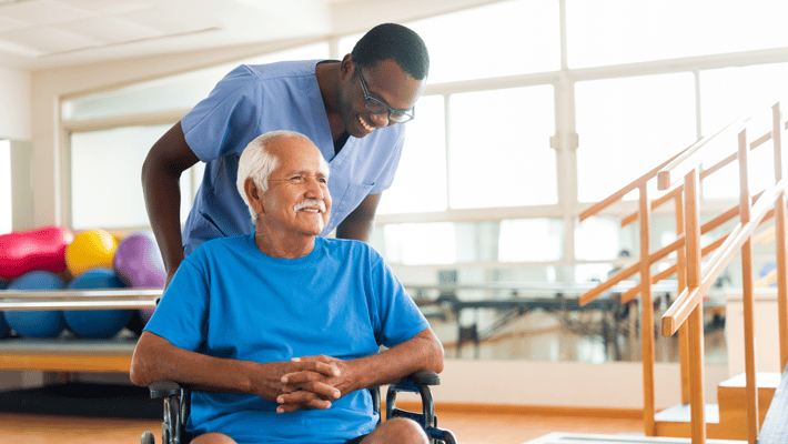 A staff member assisting an elderly resident in a therapy room