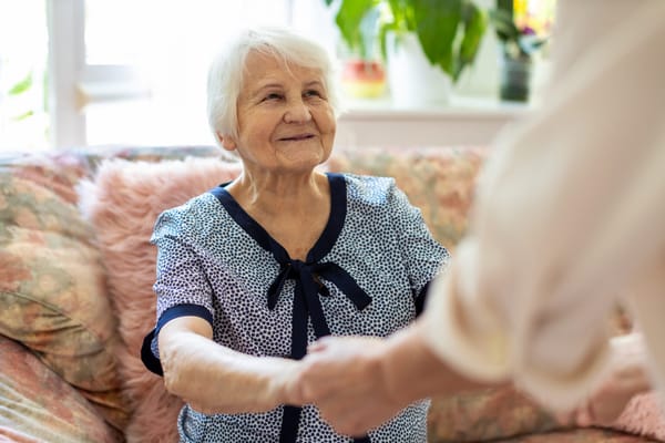 A senior woman smiling and holding hands with a caregiver