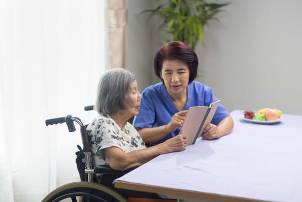 A caregiver reading with a senior resident in a bright room