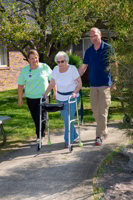 Staff assisting a resident outdoors with a walker