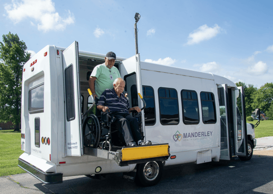 Staff assisting a resident in a wheelchair from a facility van