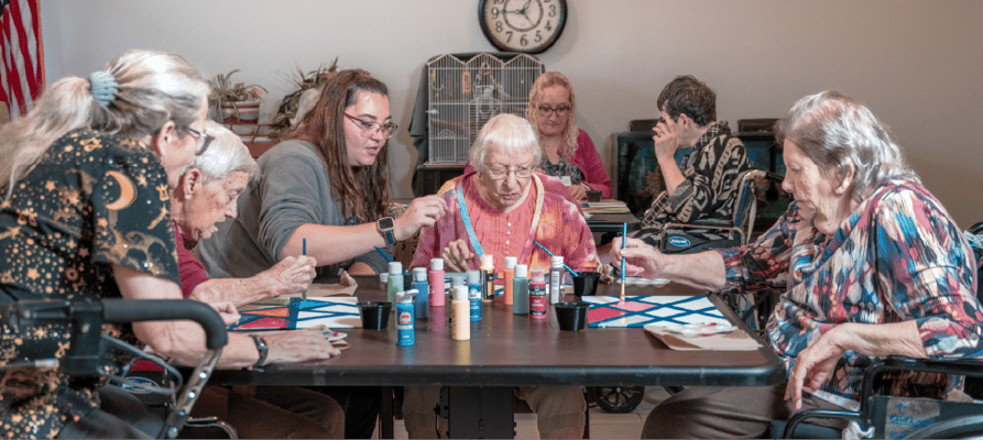 Residents painting in an activity room with staff assistance