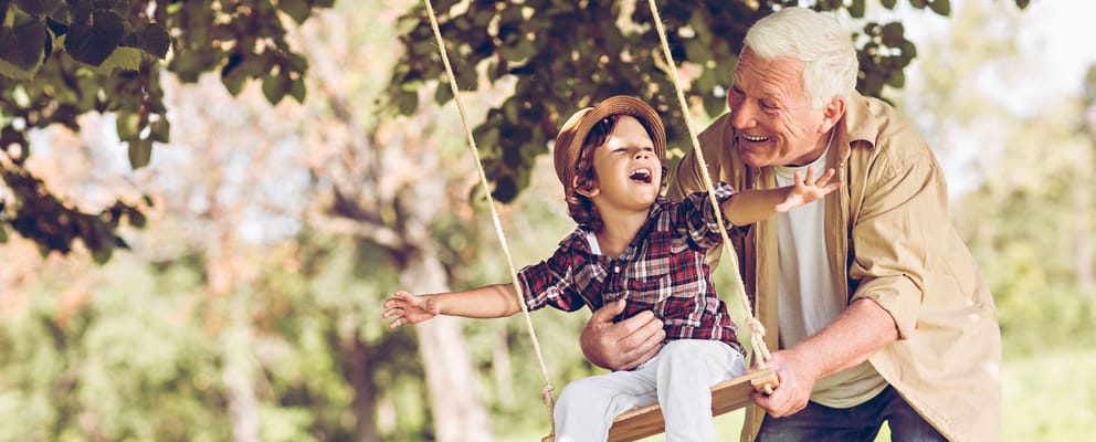 Grandfather and grandchild playing on a swing in a park