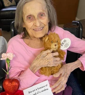 Resident smiling with a teddy bear in a cozy room