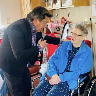 A performer singing to a smiling resident in a wheelchair