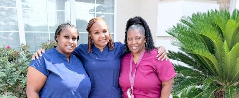 Three staff members posing outside near greenery