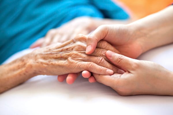 A caregiver holding an elderly person's hand