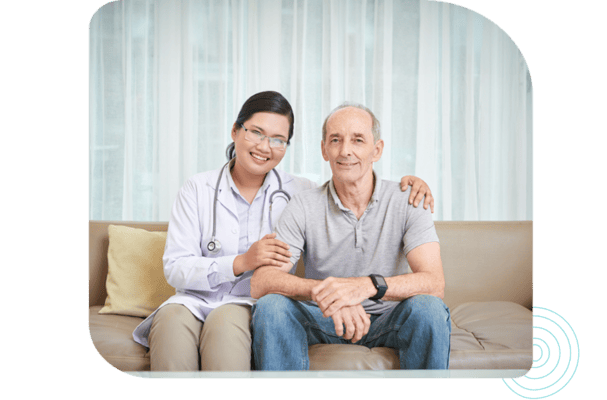 A nurse and a senior man smiling together on a sofa