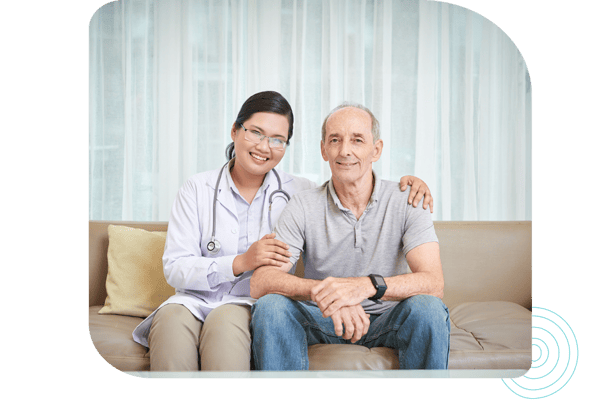 A nurse and a senior man smiling together on a sofa