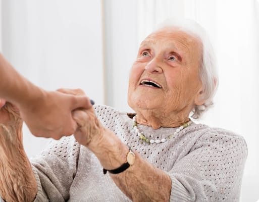 An elderly woman smiling while holding hands with a caregiver
