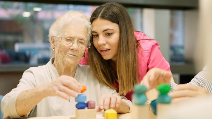 A caregiver assisting a senior resident with a stacking activity