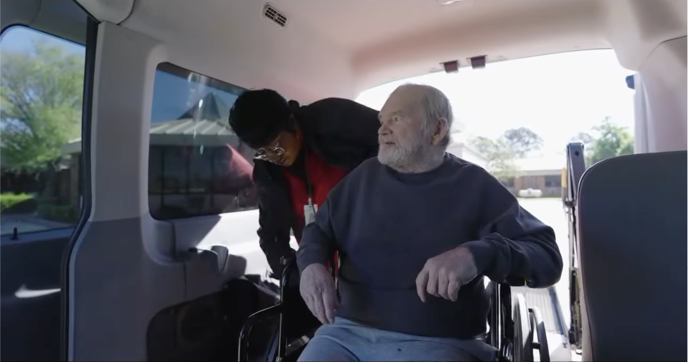 A senior man in a wheelchair with a staff member in a van
