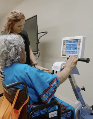 A senior resident using a therapy exercise machine with staff assistance