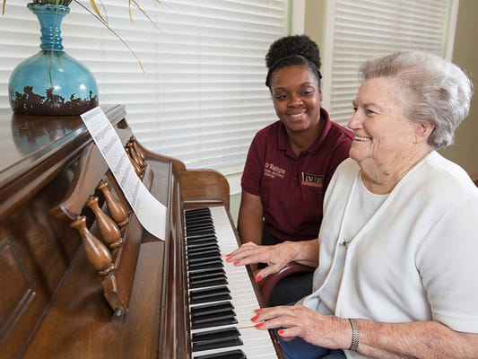 Resident playing piano with staff member in cheerful interaction