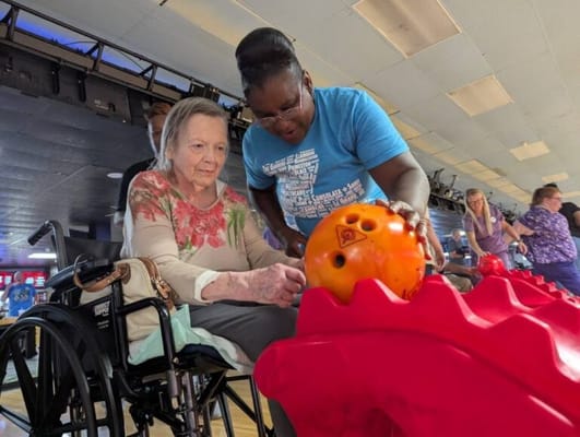 Residents bowling with staff assistance in an activity room