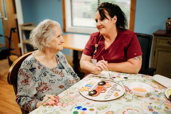 A caregiver and resident painting together during an activity