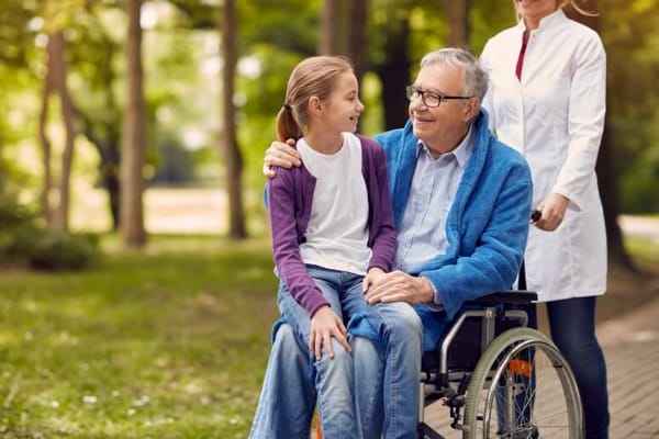 A senior man in a wheelchair enjoying time with a girl in a park