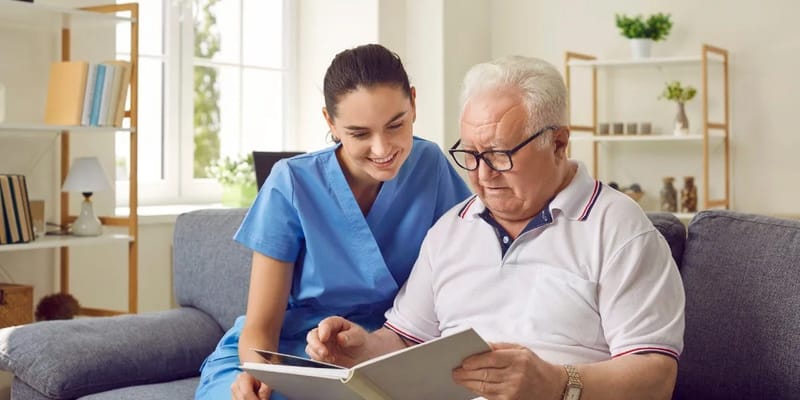 Caregiver reading with a senior man in a living room