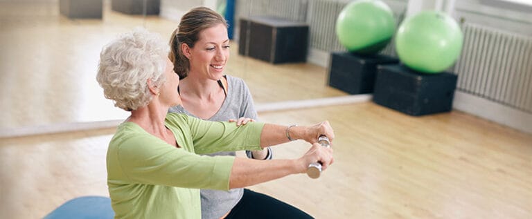 Resident exercising with a staff member in an activity room