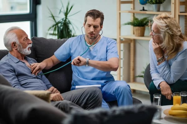 A healthcare worker checking an elderly man's health in a cozy seating area