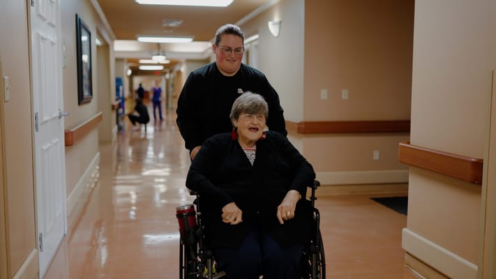 A staff member pushing a resident in a wheelchair down a hallway