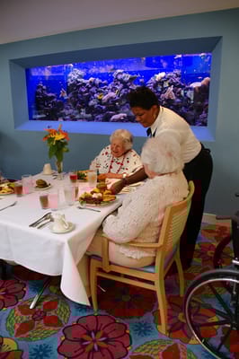Residents enjoying a meal in a dining area with an aquarium.