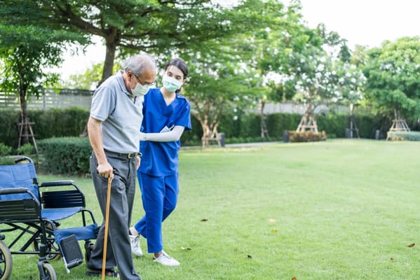 Senior man walking in a garden with staff assistance