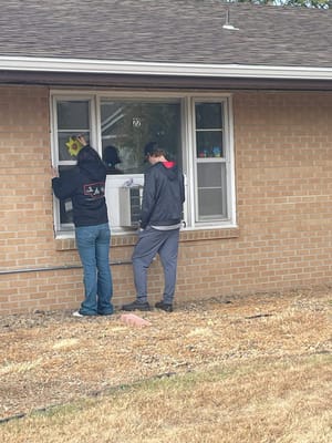 Two people decorating a window outside a facility