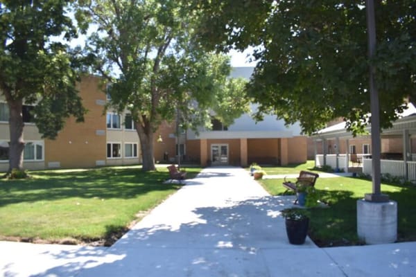 Pathway leading to a senior living facility with trees and benches