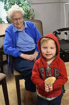 An elderly woman and a young boy holding a chick indoors