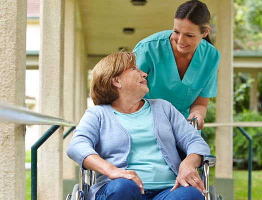 A caregiver assisting a resident in a wheelchair outside