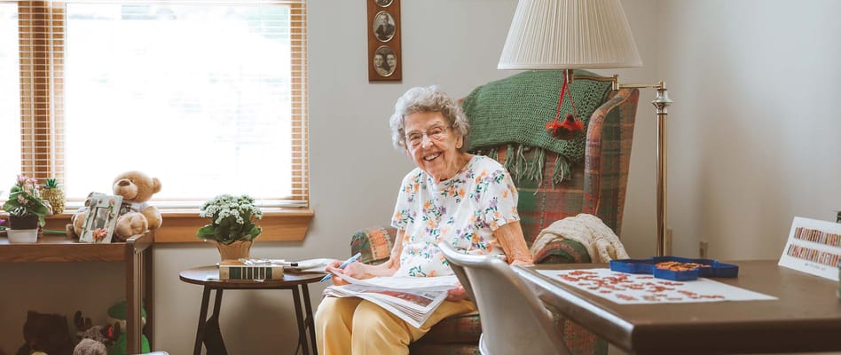 Senior resident smiling in a cozy chair with activities nearby