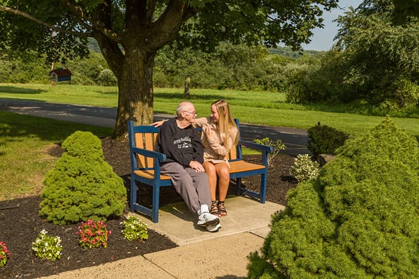 A resident and visitor sitting on a bench in a garden