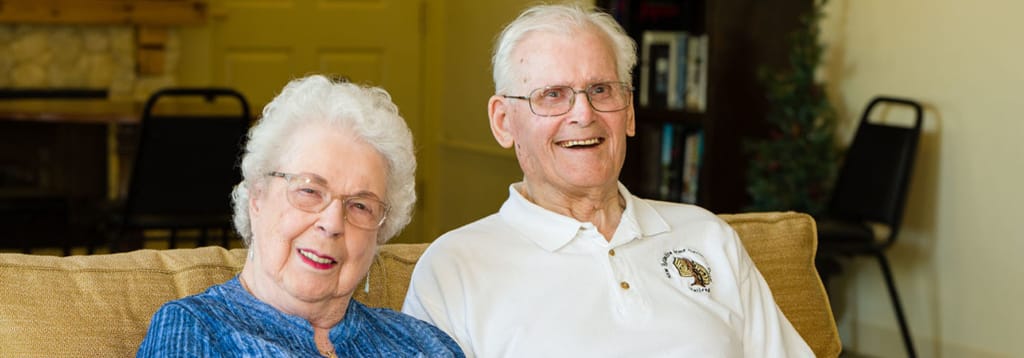 Senior couple smiling while sitting on a couch