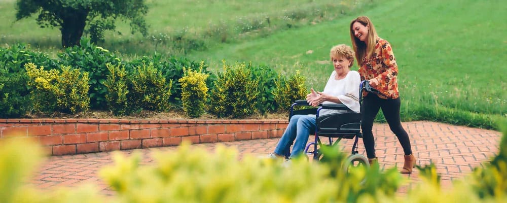 Senior resident in a wheelchair outdoors with staff