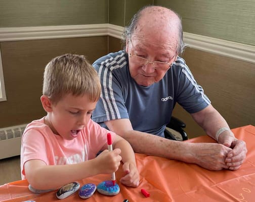 A senior and child painting together at a table