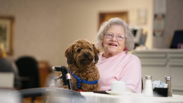 A resident smiling with a dog in a cozy setting