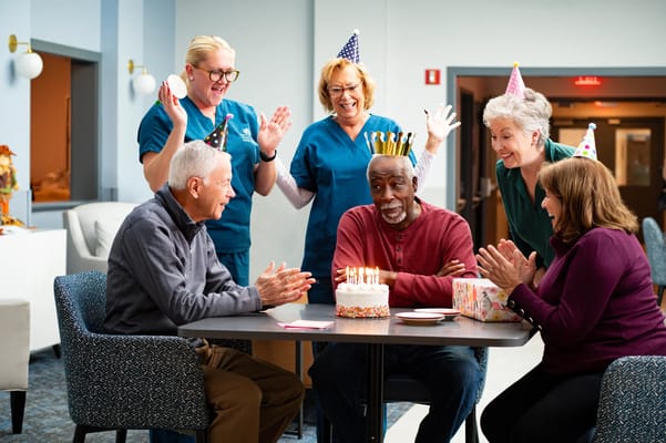 Celebration with residents and staff around a birthday cake