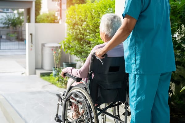 Caregiver assisting a resident in a wheelchair outdoors