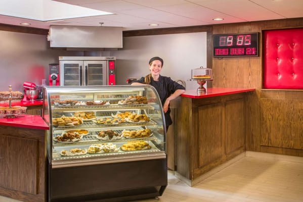 A staff member next to a bakery display in a dining area
