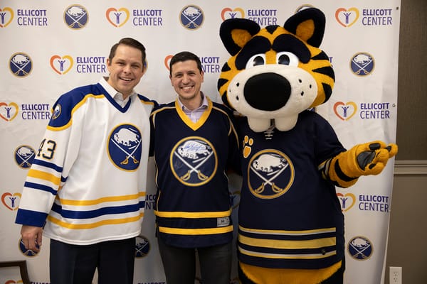 Two men in hockey jerseys with a mascot in a social event