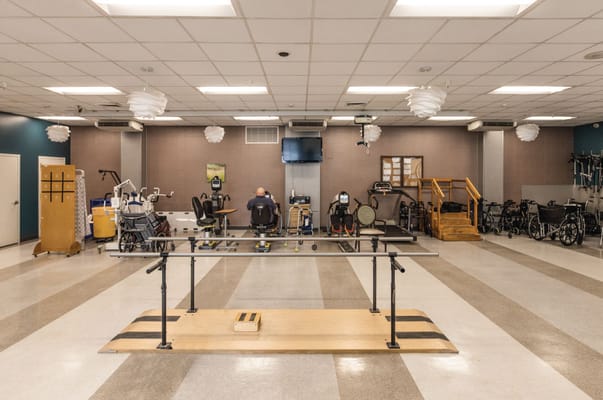 A rehabilitation room with equipment and a therapist assisting a resident