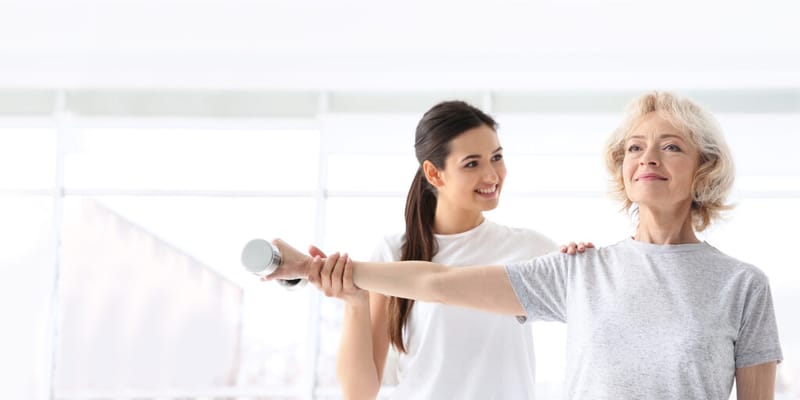 A staff member assisting a senior woman with exercise