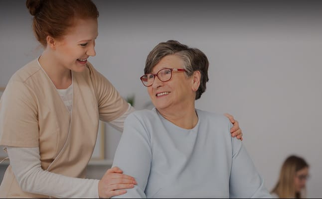 Caregiver assisting a smiling resident in a light-filled room