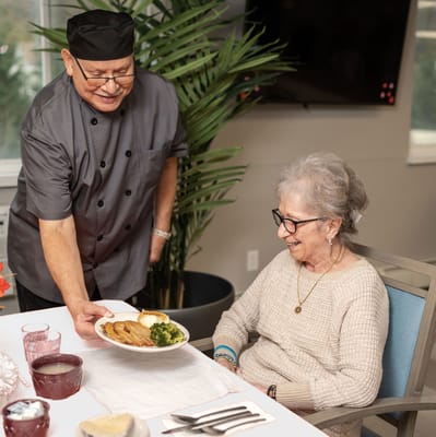 Senior resident enjoying a meal served by staff