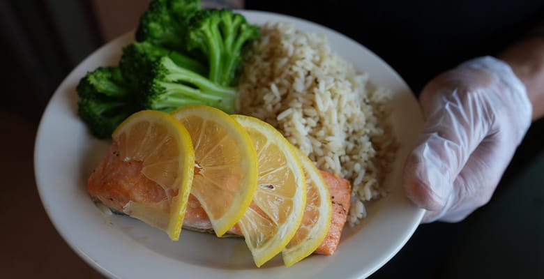 Plate of salmon with lemon and broccoli served by staff