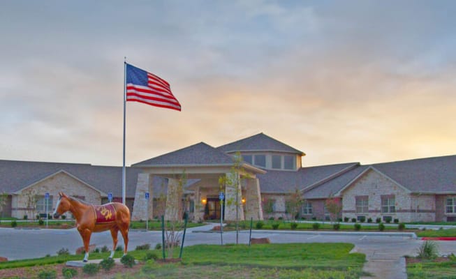 Exterior view of a senior living facility with a flag and horse statue