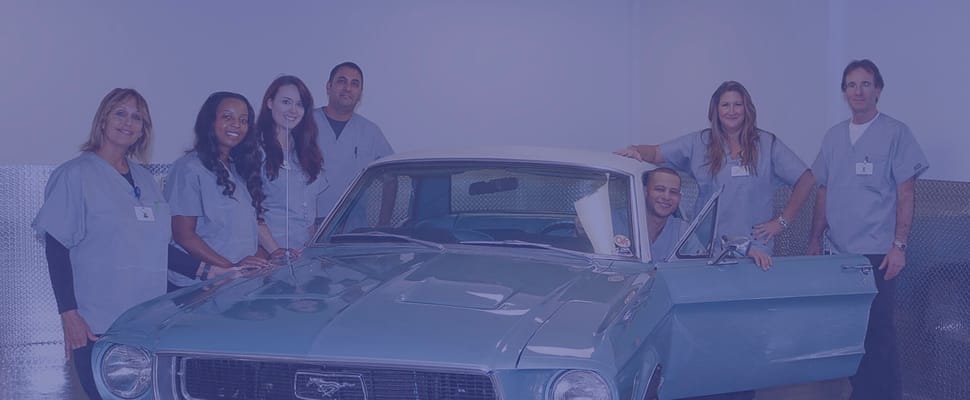 Staff with residents by a classic car in a facility