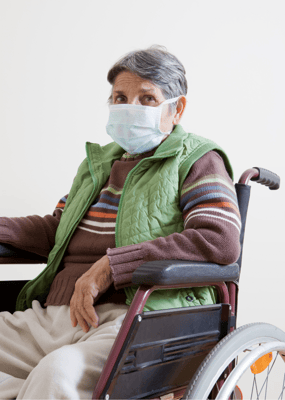 An elderly woman in a wheelchair wearing a mask