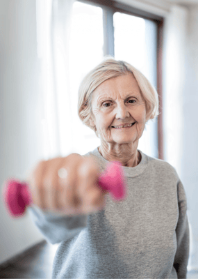Senior woman exercising with a pink dumbbell indoors